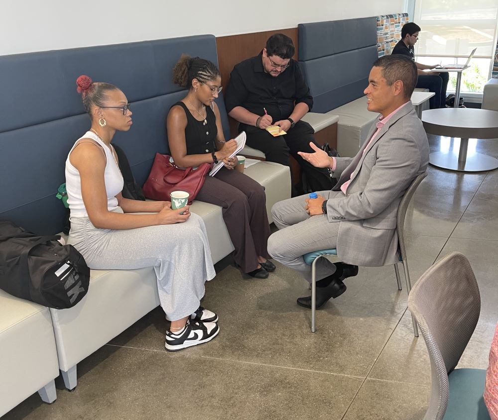A recruiter for Marriott sits in H-Cafe with three students while they take notes and drink coffee.