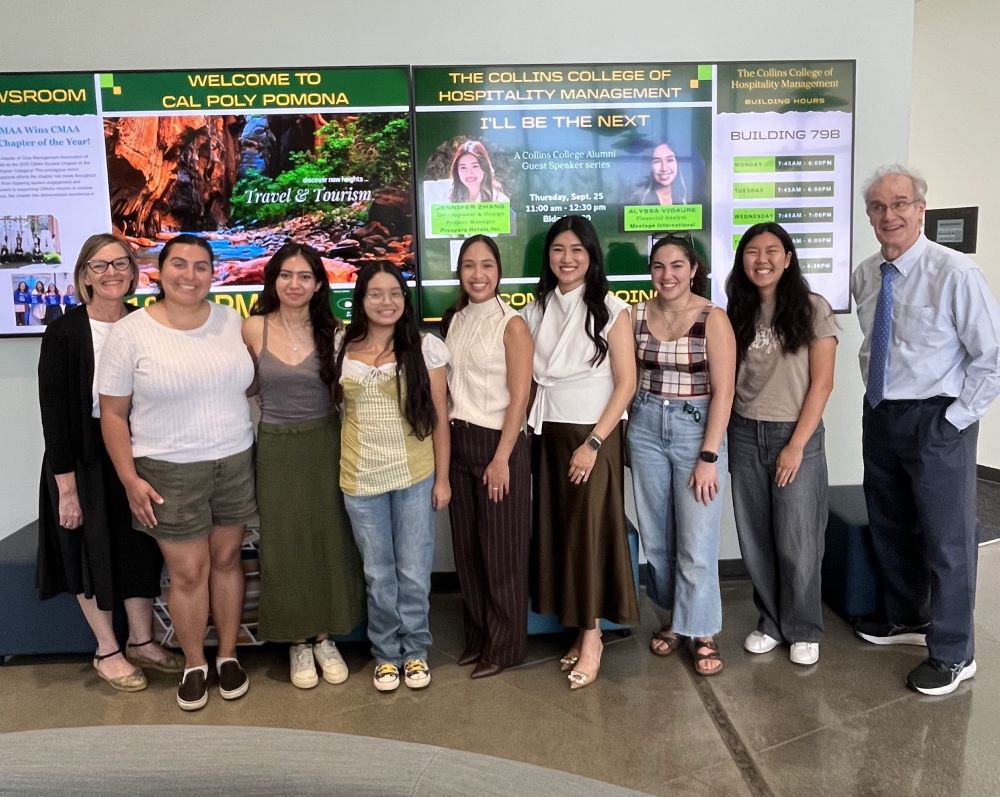 A group of people stand in front of large digital screens in Building 80 with alumni speakers Alyssa Visaure and Jennifer Zhang. 