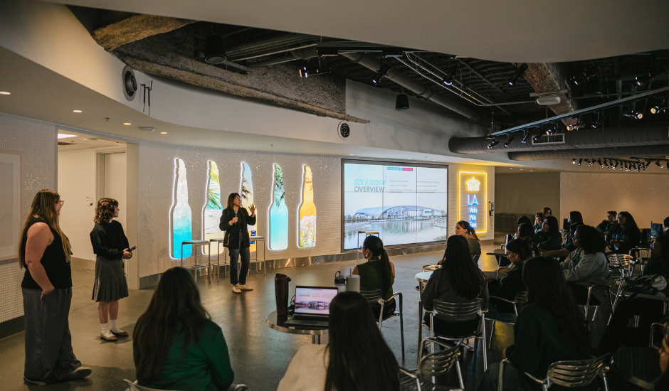 Students on field trip attending presentation in SoFi Stadium event space with large screen