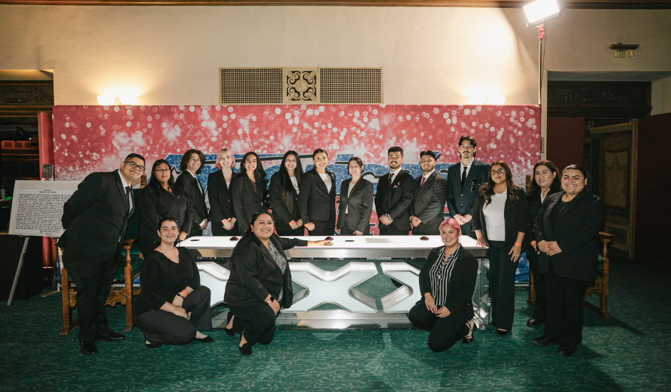 Students on field trip posing behind an X factor table indoors