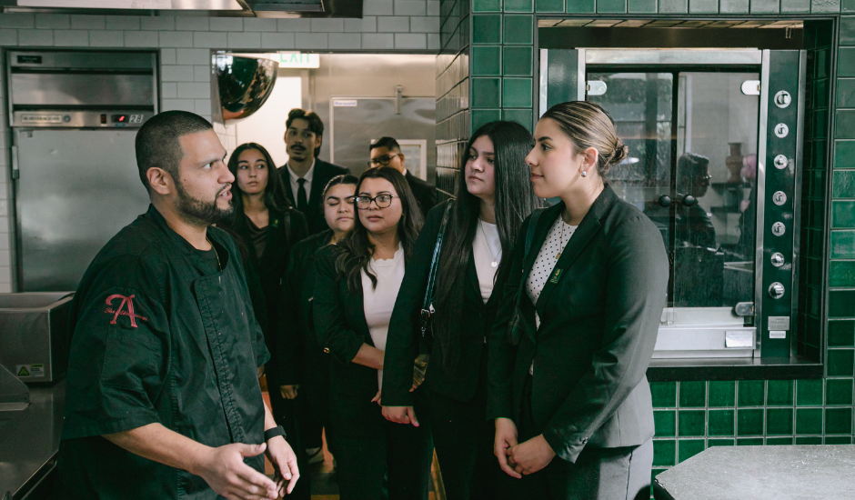 Students on field trip listening to chef in tiled kitchen area at The Athenaeum