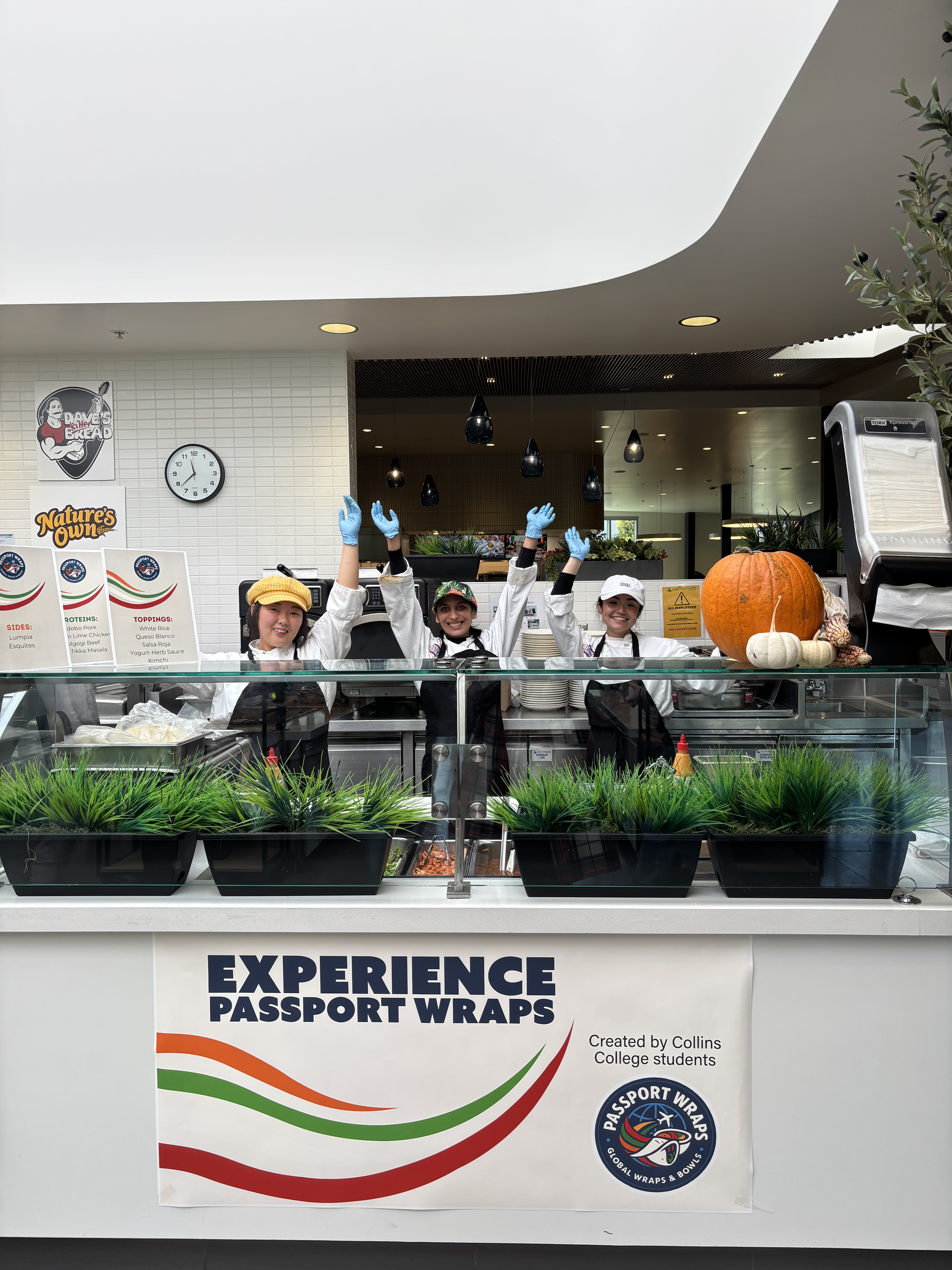 Passport Wraps group photo behind the counter with arms raised.