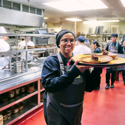 A server in the kitchen carrying a tray of food to the dining room.