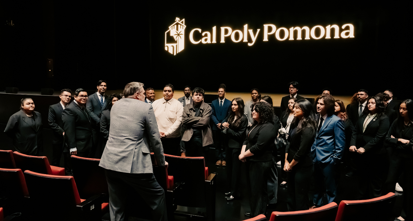 Students inside the theatre at Yamavaa listening to a man speak with a projection of the cal poly pomona logo visible in the background