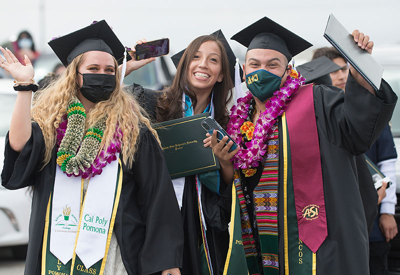 Two graduates wear a mask while the third graduate does not