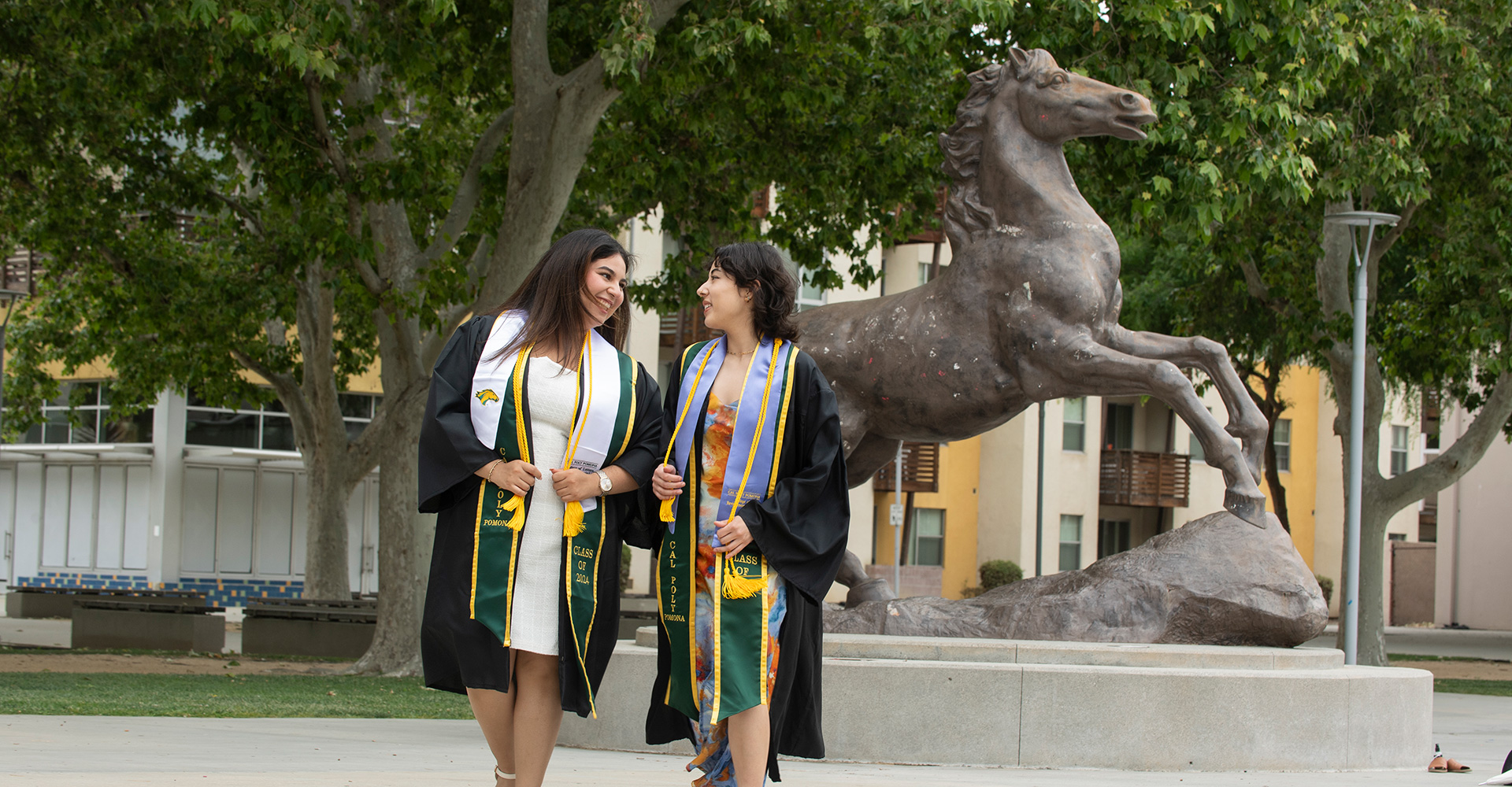 Two female graduates by the Bronco Statue