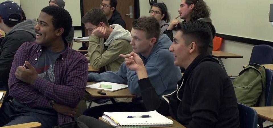 students in classroom discussing, one pointing towards the board