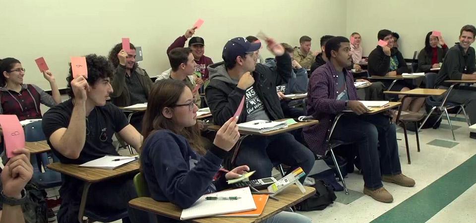 students in classroom holding cards and raising their hands