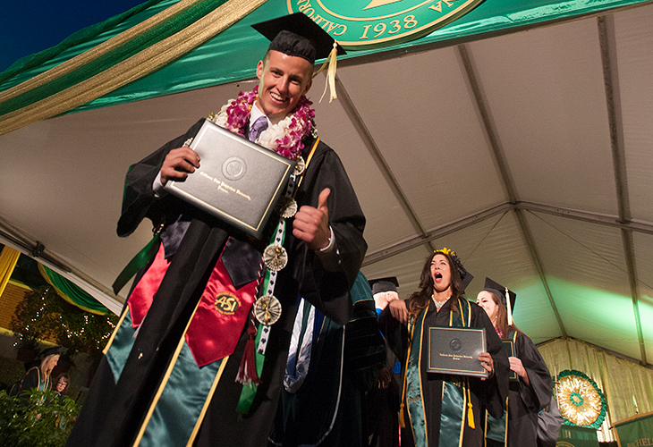 Diverse group of professionals smiling and collaborating around a table with laptops and a tablet in a modern office setting