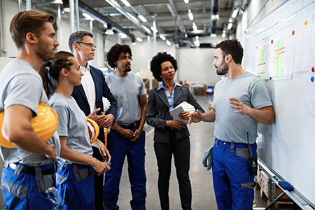 people meeting and standing in front of a white board