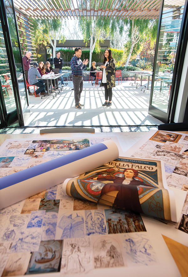 Barbara Bouza in the distance speaking with an colleague with a layout of Amelia Falco posters and fabrics. 