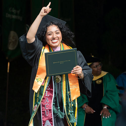 Female student lifts hand in celebration during commencement while holding diploma