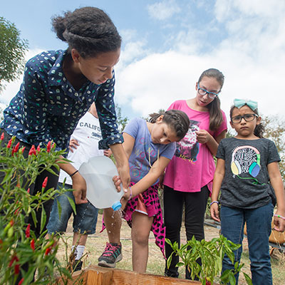 A female student works with a child watering a garden