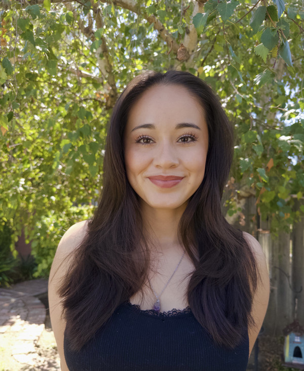 Isabella posing outdoors on a sunny day with a tree behind her.