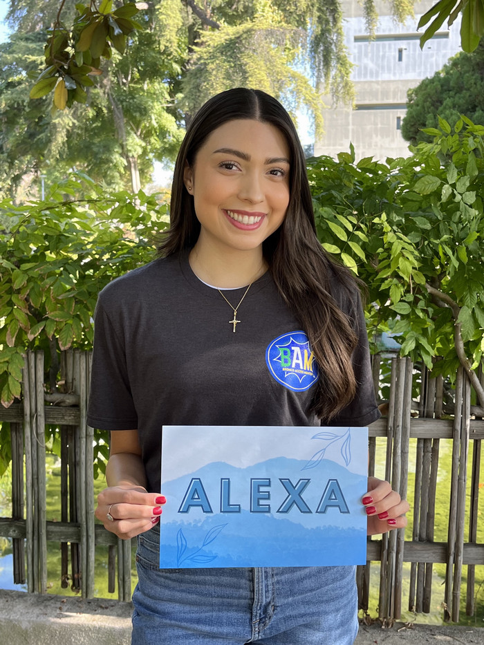 Alexa posing in a BAM shirt with a sign with her name on it.