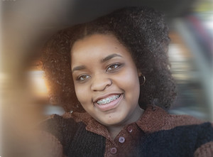 Aliya is smiling in an artistic photo with the background blurred.