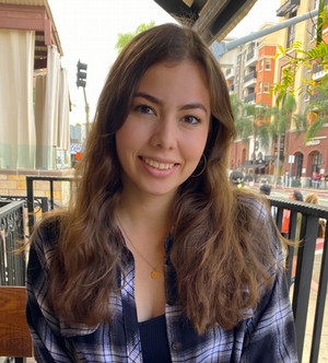 Stephanie is sitting at a table near a city street.