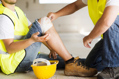 Construction worker with injured knee sat down being assisted by co-worker