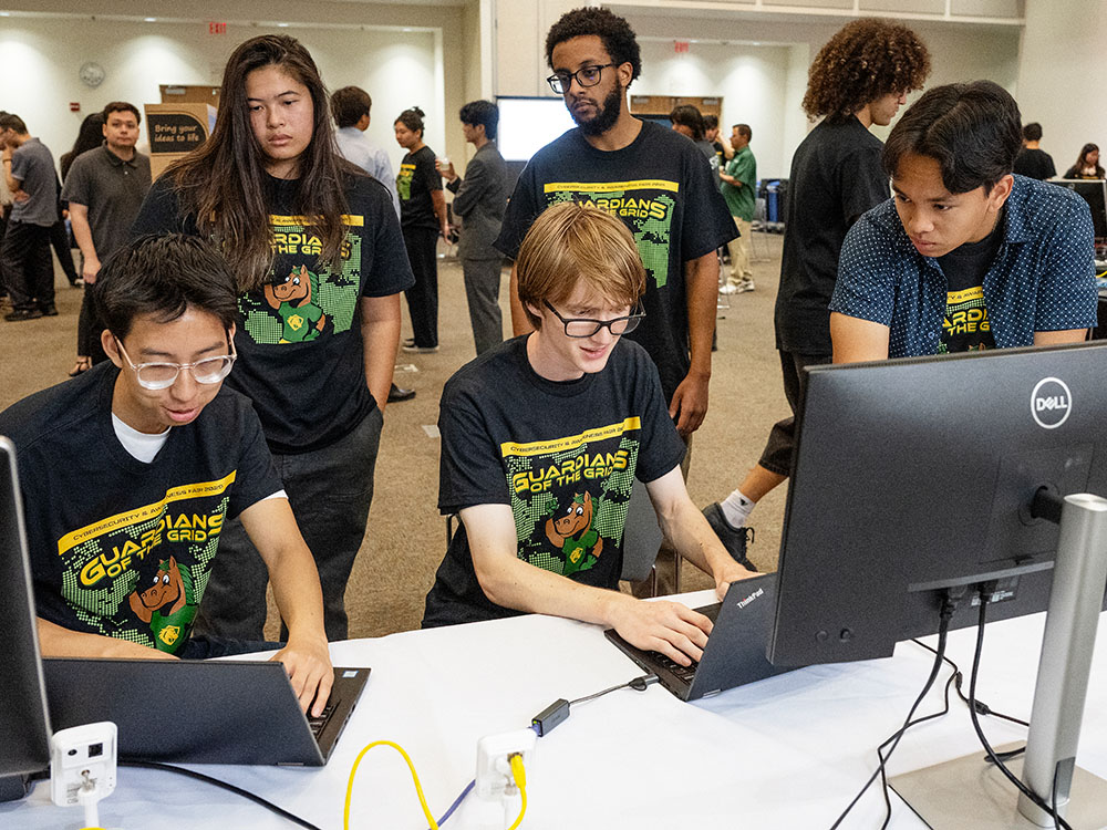 five students, standing, looking at a computer screen