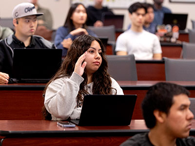 A student raises her hand in a lecture hall