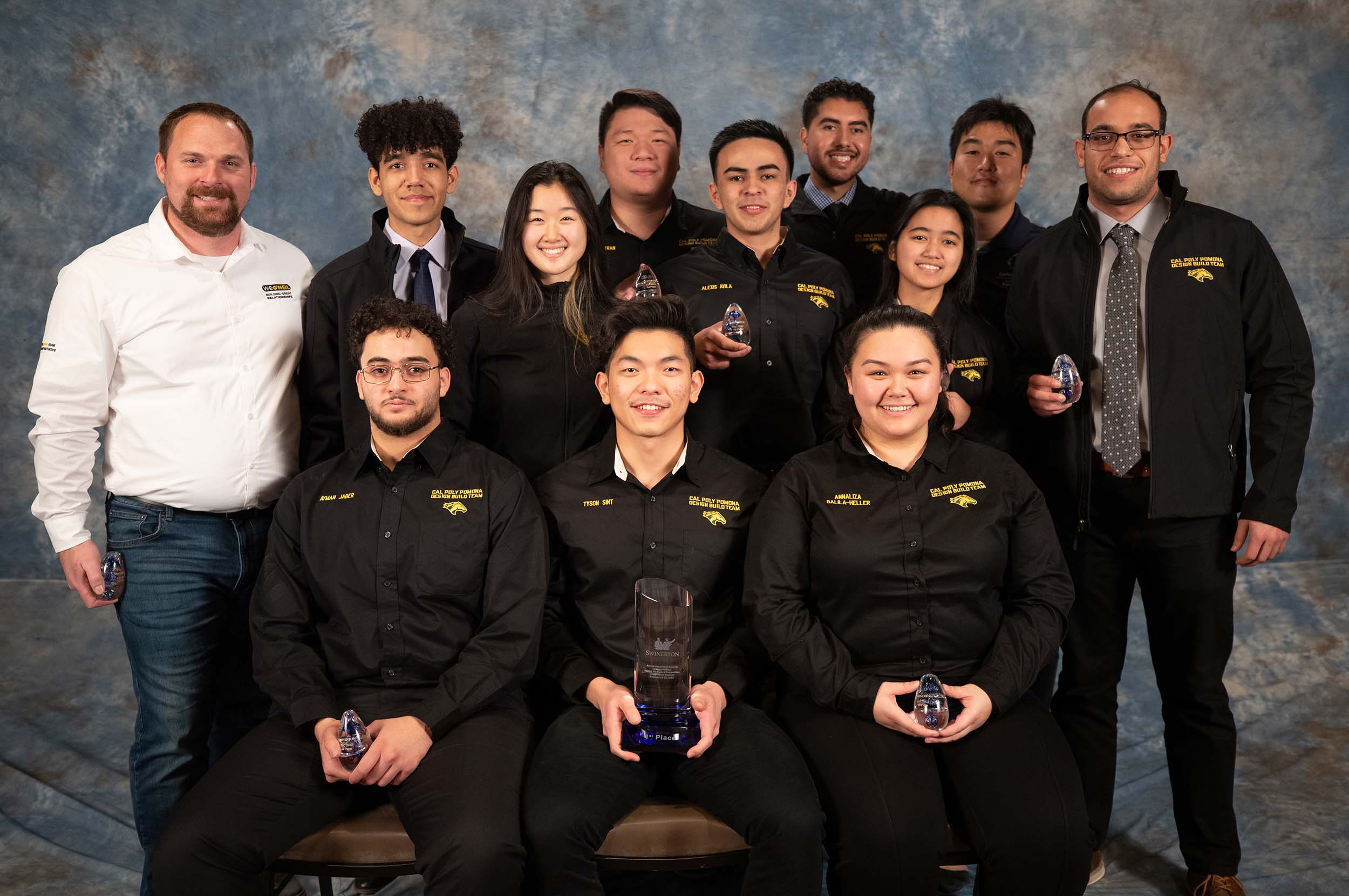 A group photo of a dozen people, 10 of them students, holding awards for a student competition victory.