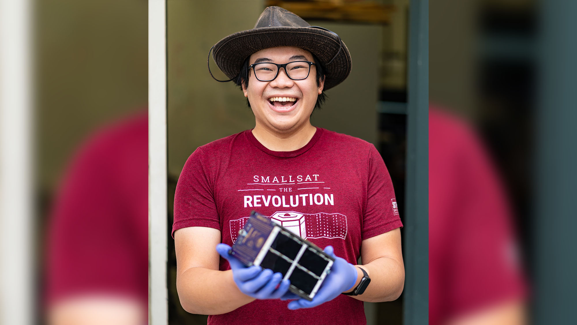 A photo of a CPP Engineering student smiling and holding a miniature satellite.