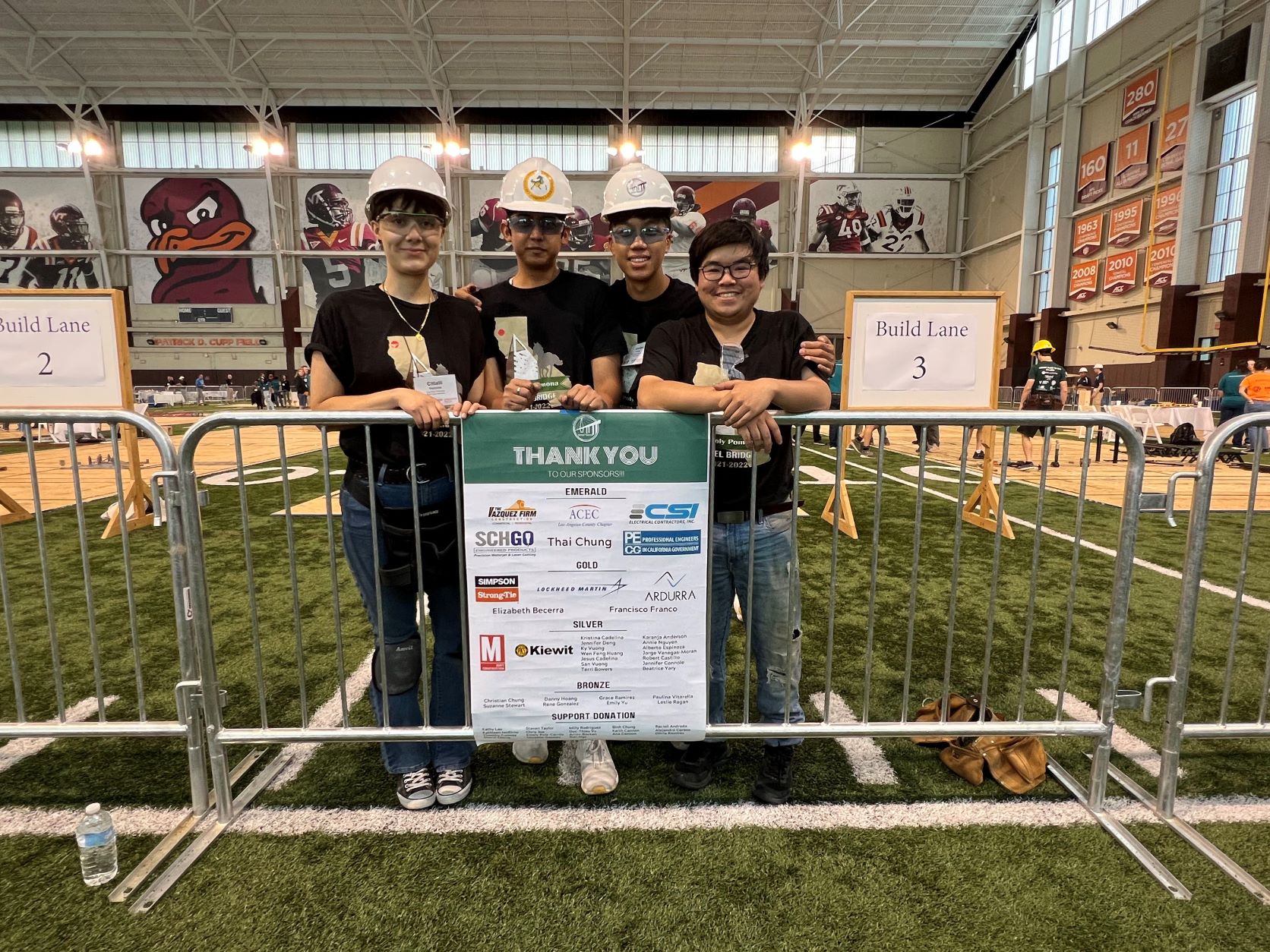 A group photo of four students with hard hats celebrating their victory in a student competition.