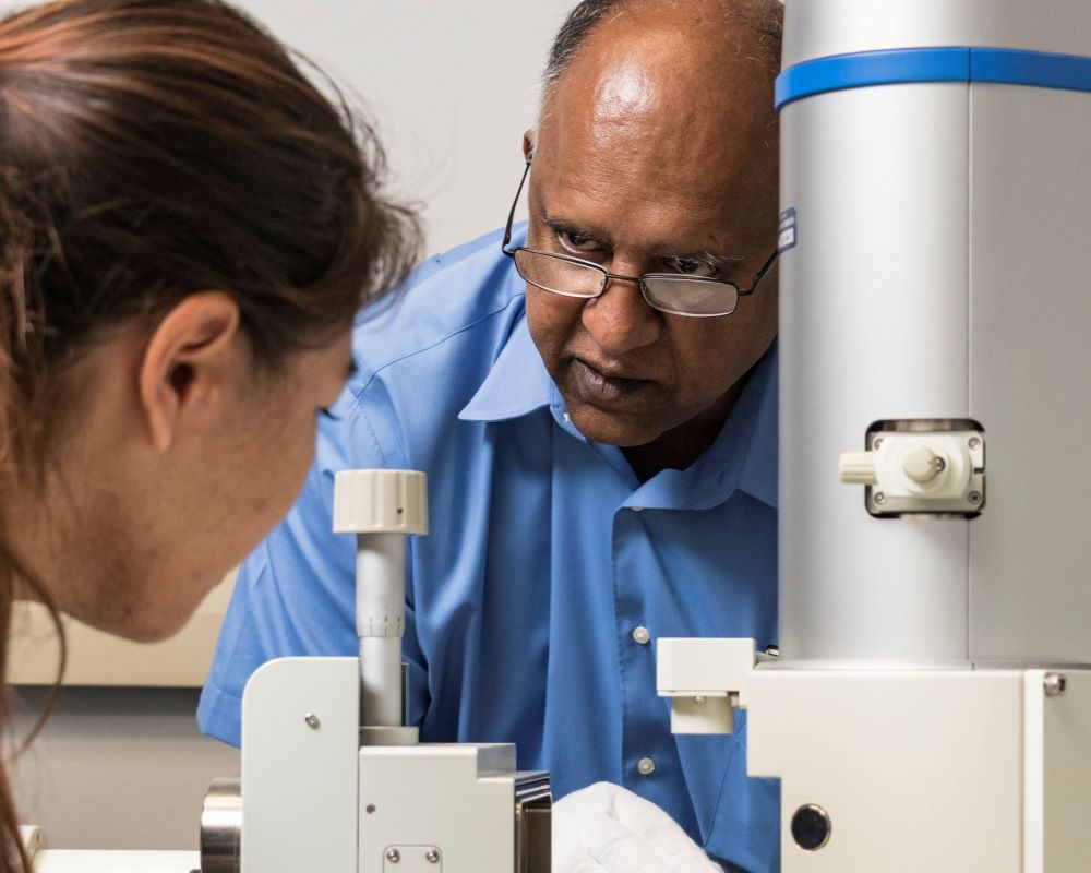 Professor Vilupanur Ravi teaching a student how to operate a scanning electron microscope.