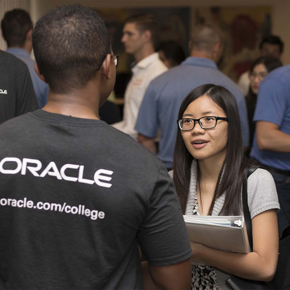 An job recruiter from Oracle speaks with a student. "Oracle" is on the back of the recruiter's shirt.