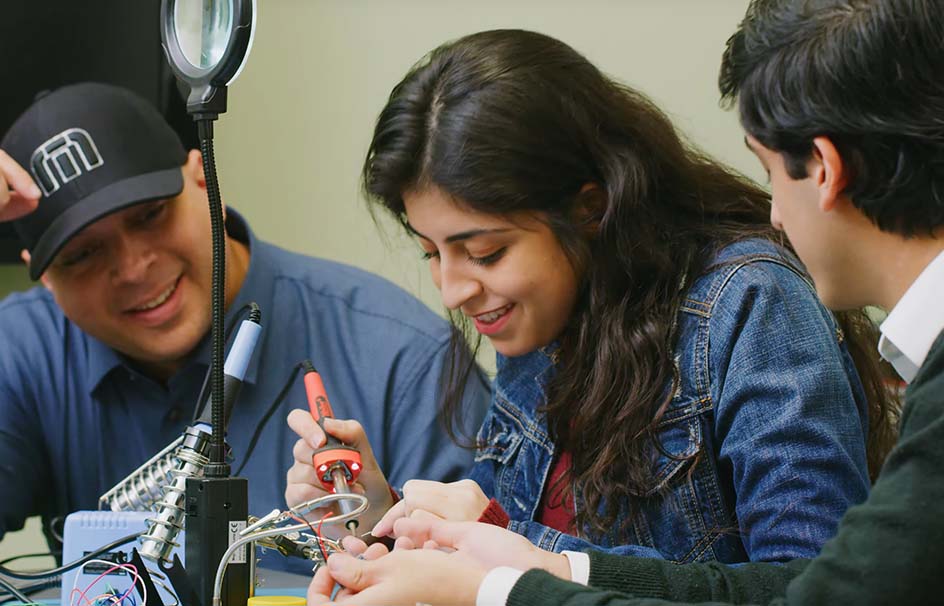 A female engineering student works on a projects as two male students observe her work