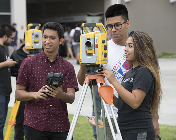 One female and two male engineering students using a civil engineering survey tool.