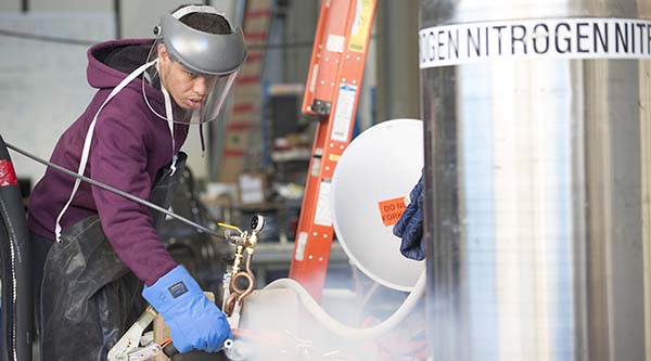 An engineering student working with liquid nitrogen. Nitrogen is written on a metal tank.