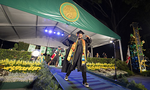 An engineering student in commencement regalia walking down the steps as he recieves his diploma cover.