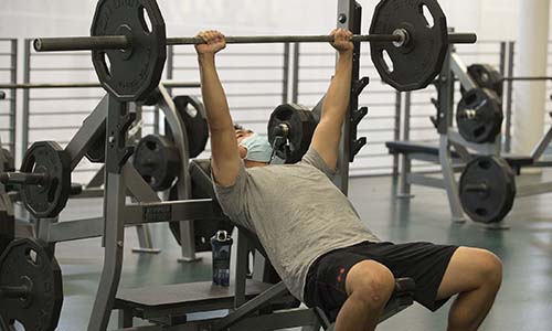 A college student lifting a barbell in a gym.