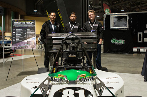 Three male engineering students standing behind their Formula race car.