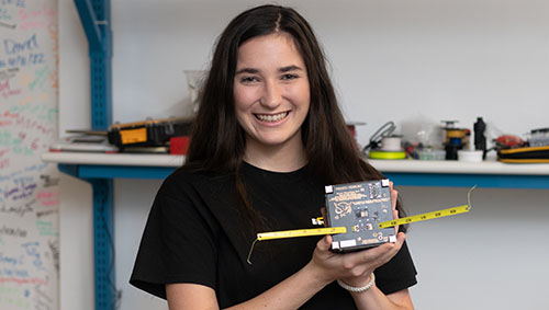CPP Engineering student Megan Beck holding a CubeSat, a miniature satellite.