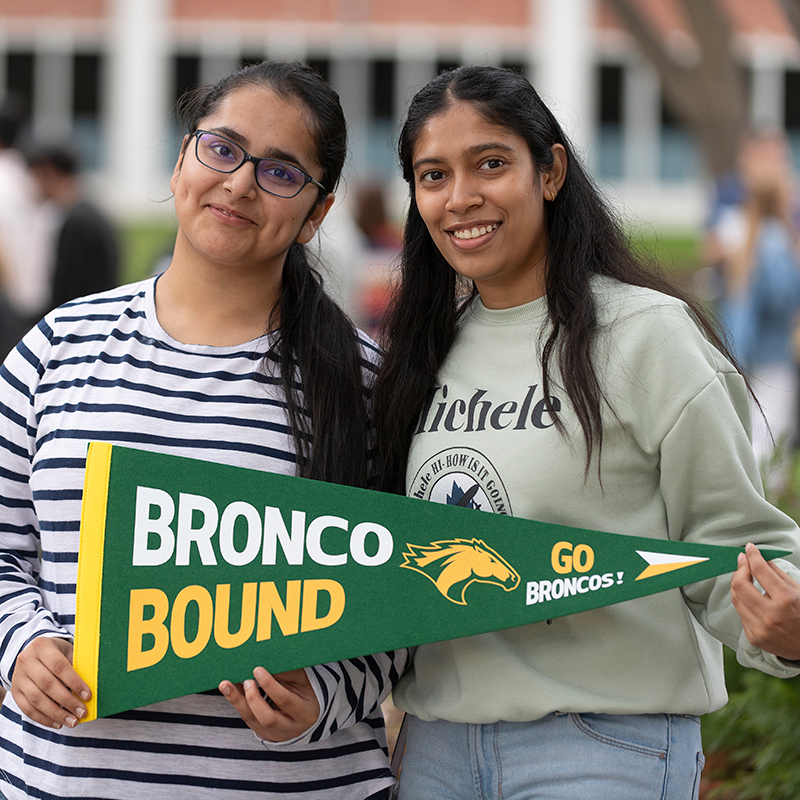 A mother and daughter smile while holding a BroncoBound flag. 