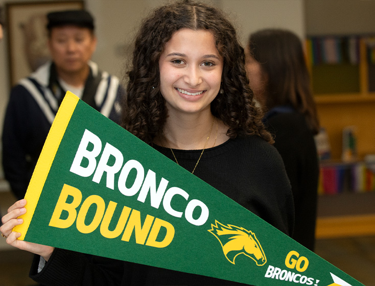 A girl smiles with a pennant in her hands with the text "Bronco Bound"