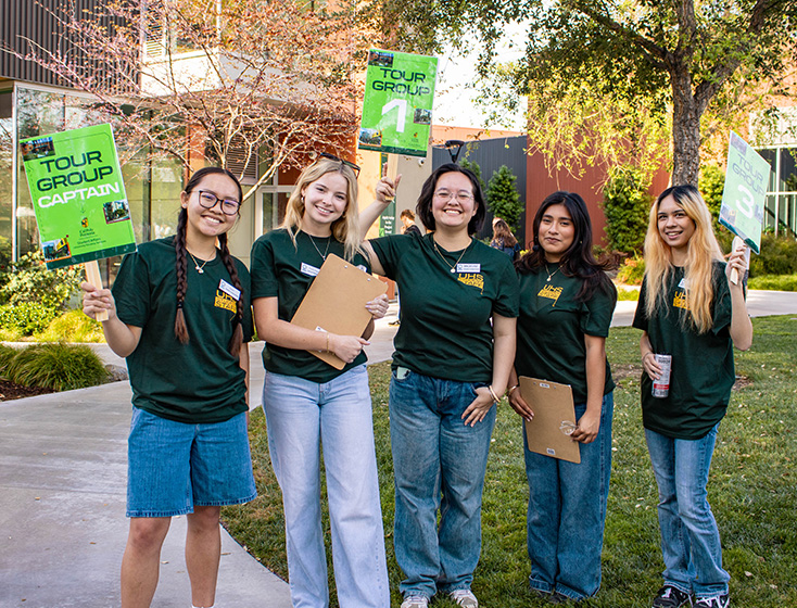 A team of tour guides for University Housing smile with their tour group signs. 