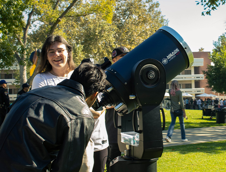 A student peeks through a large telescope at the sky at the Explore CPP Resource Fair.
