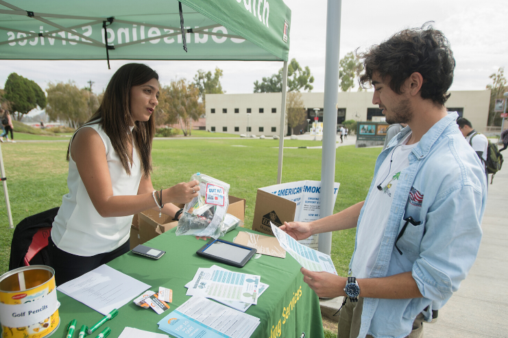 A Student Health staff member hands a student an information bag at a tabling event