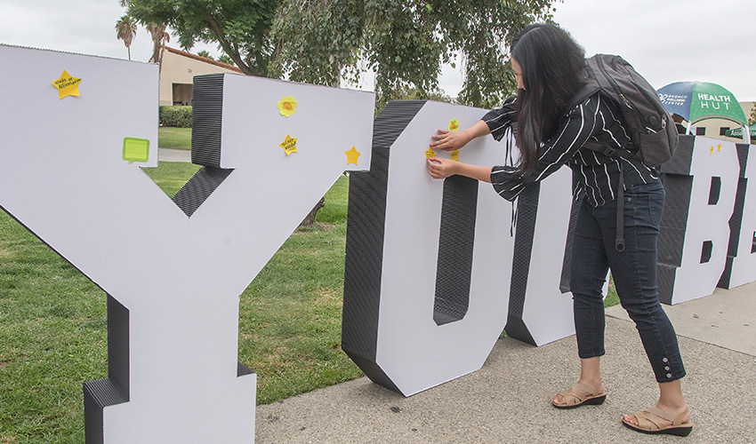 A student stick a post it on the You Belong sign on campus. 
