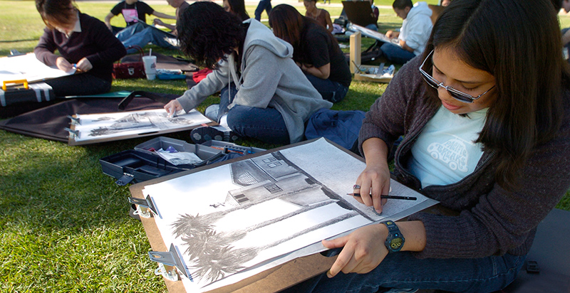 students sitting on the grass drawing