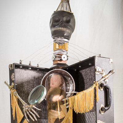 Gina M.  In A Dream from the Toy Box Kids Series, 2018  assemblage, ceramic skull, doll, plastic tube, magnifying glass, drum stand table, movie reel winders, fringe, found parts   68 x 24 x 24”  Courtesy of the artist