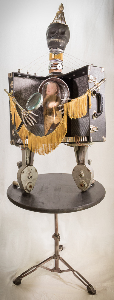 Gina M.  In A Dream from the Toy Box Kids Series, 2018  assemblage, ceramic skull, doll, plastic tube, magnifying glass, drum stand table, movie reel winders, fringe, found parts   68 x 24 x 24”  Courtesy of the artist