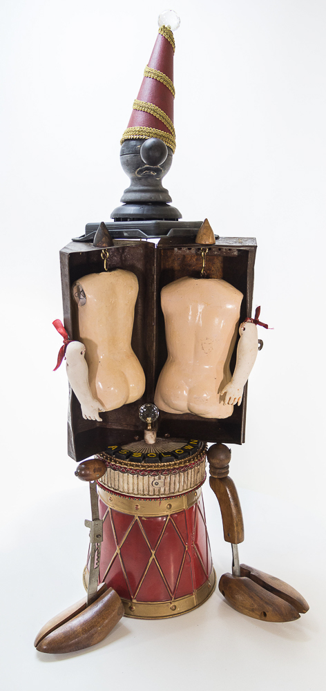 Gina M.  Ass Clown from the Toy Box Kids Series, 2018  assemblage, doll bodies, rusty box, scrabble letters, shoe horns  36 x 14 x 17”  Courtesy of the artist