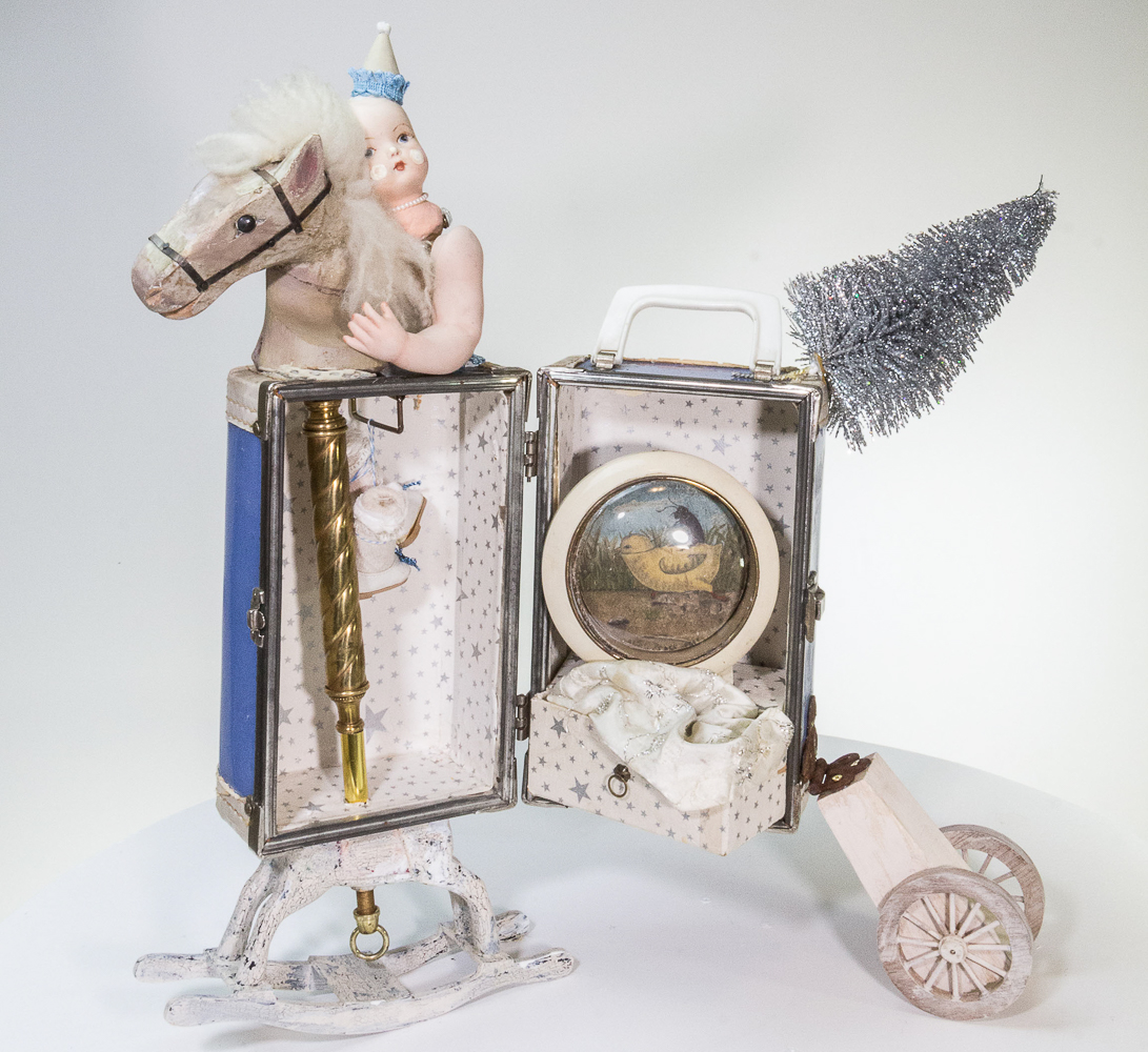 Gina M.  My Little Pony from the Toy Box Kids Series, 2018  assemblage, blue doll trunk, doll parts, clock case, silver tree, postcard, doll clothes  22 x 24 x 12”  Courtesy of the artist