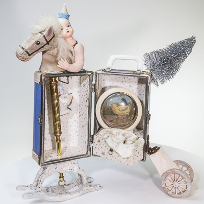 Gina M.  My Little Pony from the Toy Box Kids Series, 2018  assemblage, blue doll trunk, doll parts, clock case, silver tree, postcard, doll clothes  22 x 24 x 12”  Courtesy of the artist