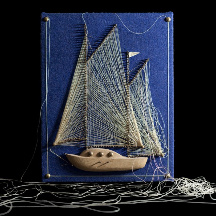 Blue fabric canvas with boat embroidered into it with string on the floor