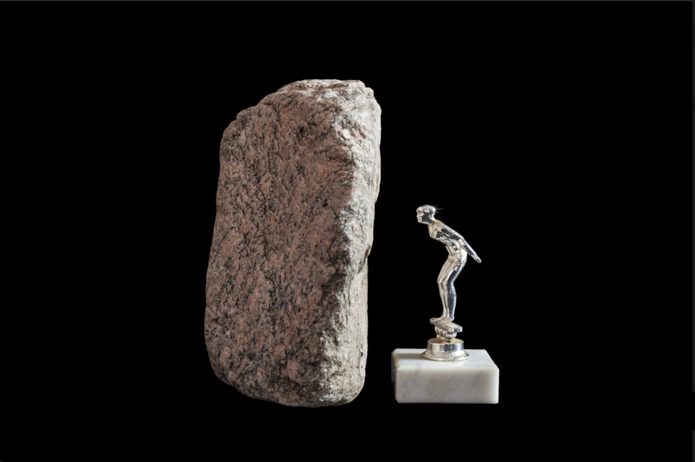 vertical rock next to a trophy of a man faced towards the rock 